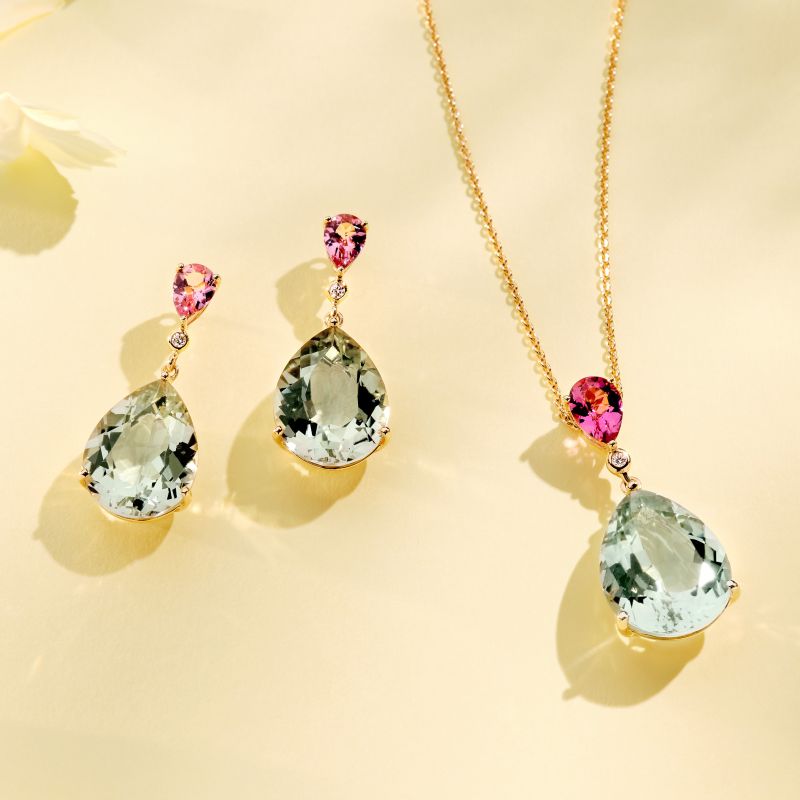 18ct yellow gold drop earrings and necklace with pear shaped pink tourmalines, round diamonds and pear shaped green amethysts, displayed on a pale yellow background.